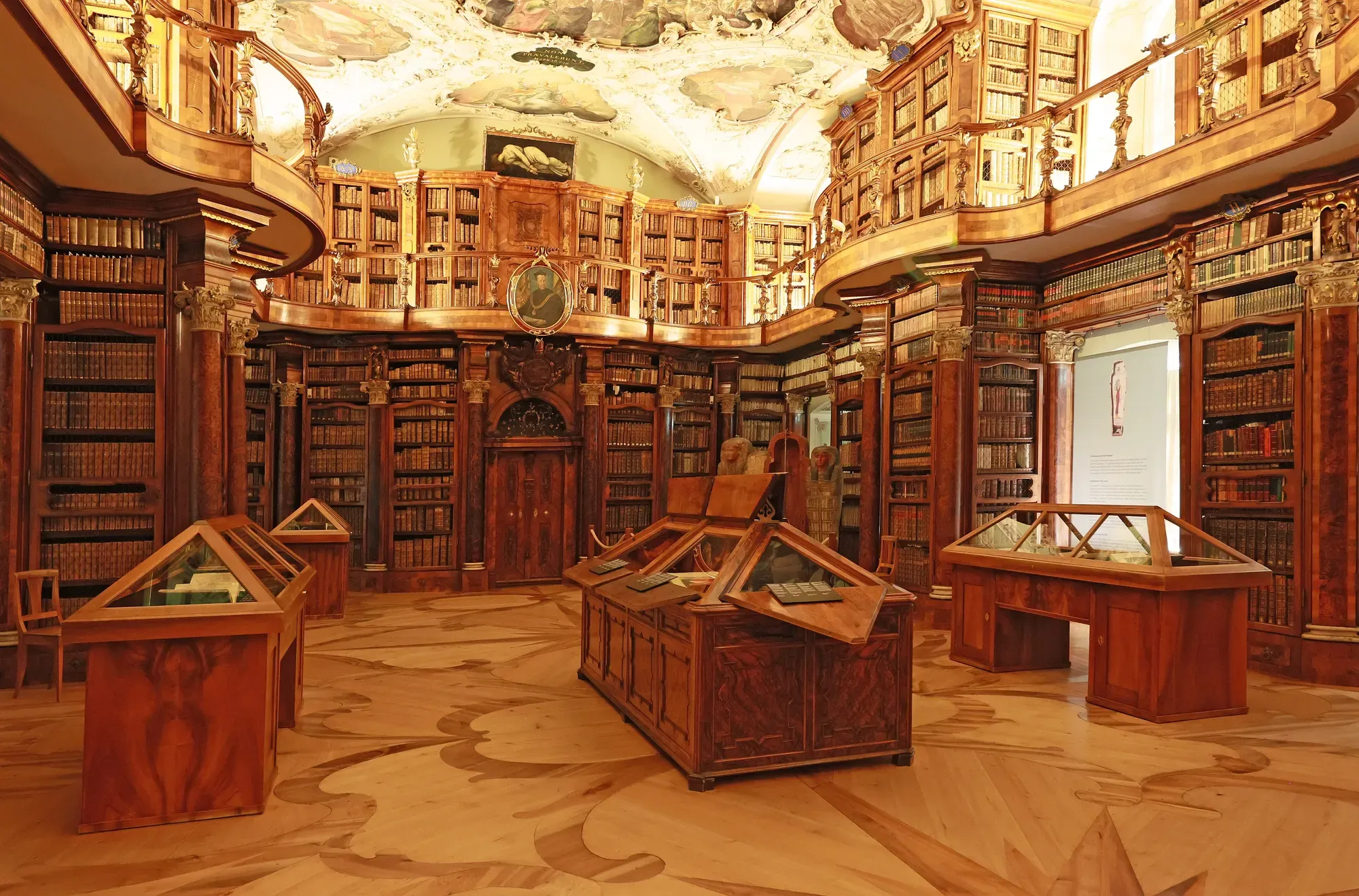The baroque hall of the St. Gallen abbey library, with carved wooden bookcases, a gallery, display cases and an inlaid wooden floor
