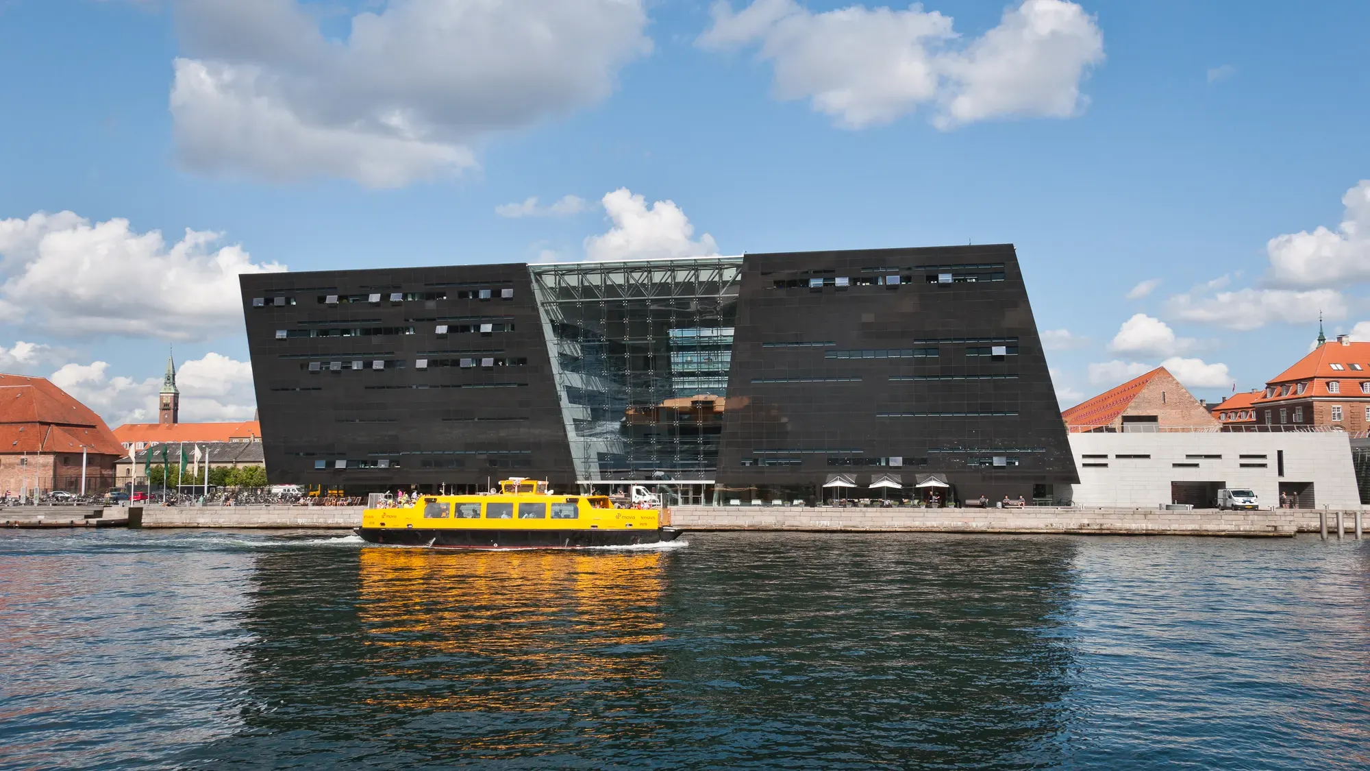 The Black Diamond on Copenhagen's harbour, a black, angled block split by a band of glass, with a yellow harbour bus in front