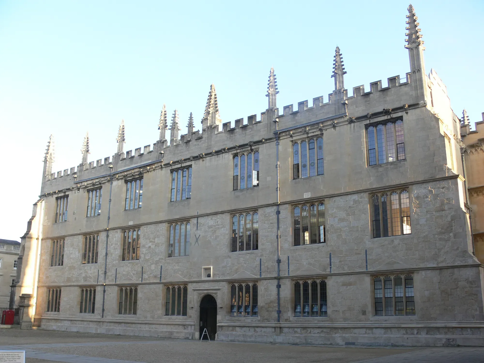A Gothic stone façade of the Bodleian Library in Oxford, its roofline lined with carved pinnacles
