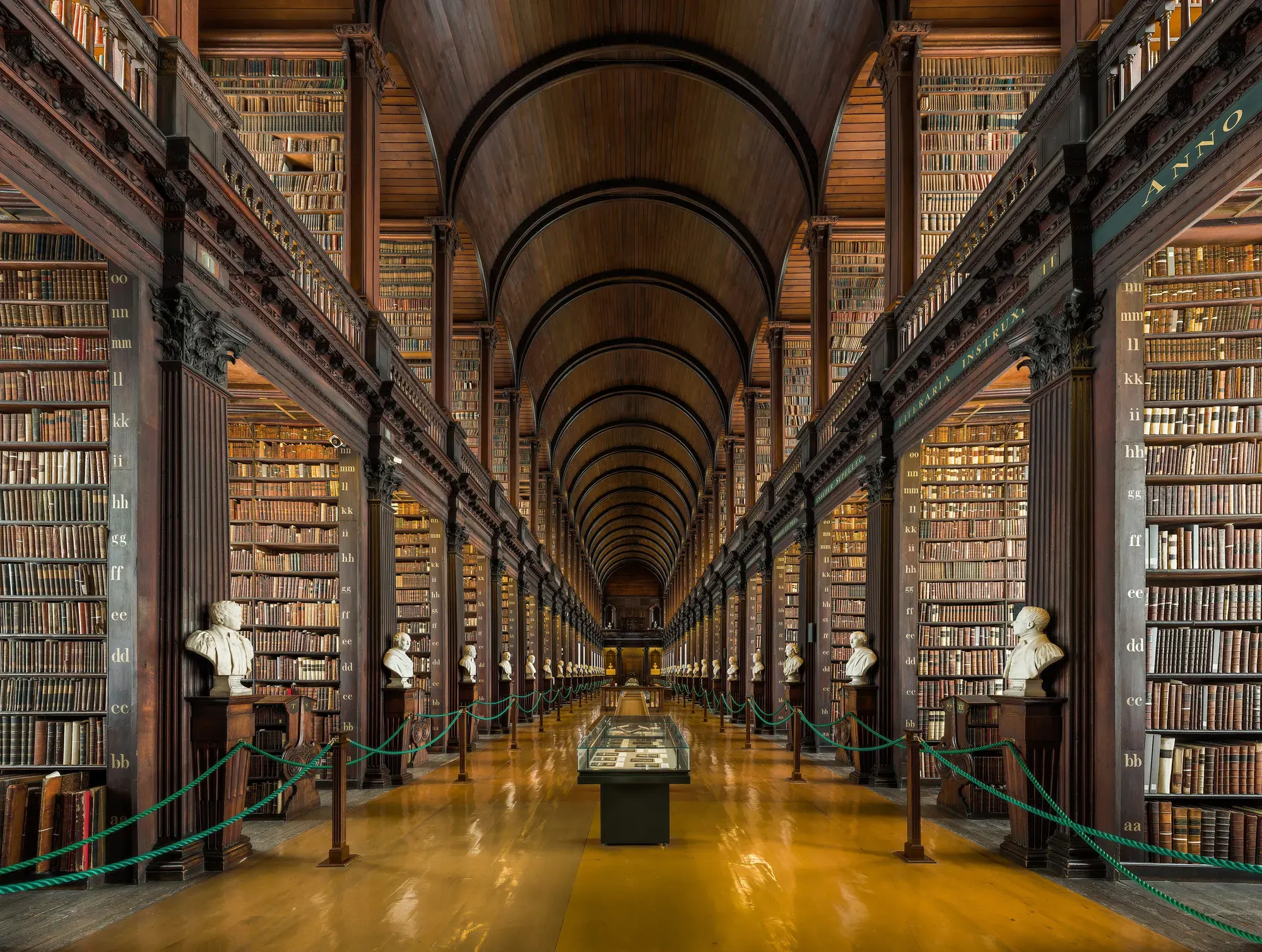 The Long Room at Trinity College Dublin: a barrel-vaulted timber ceiling over two tiers of oak bookcases, with marble busts along the aisle
