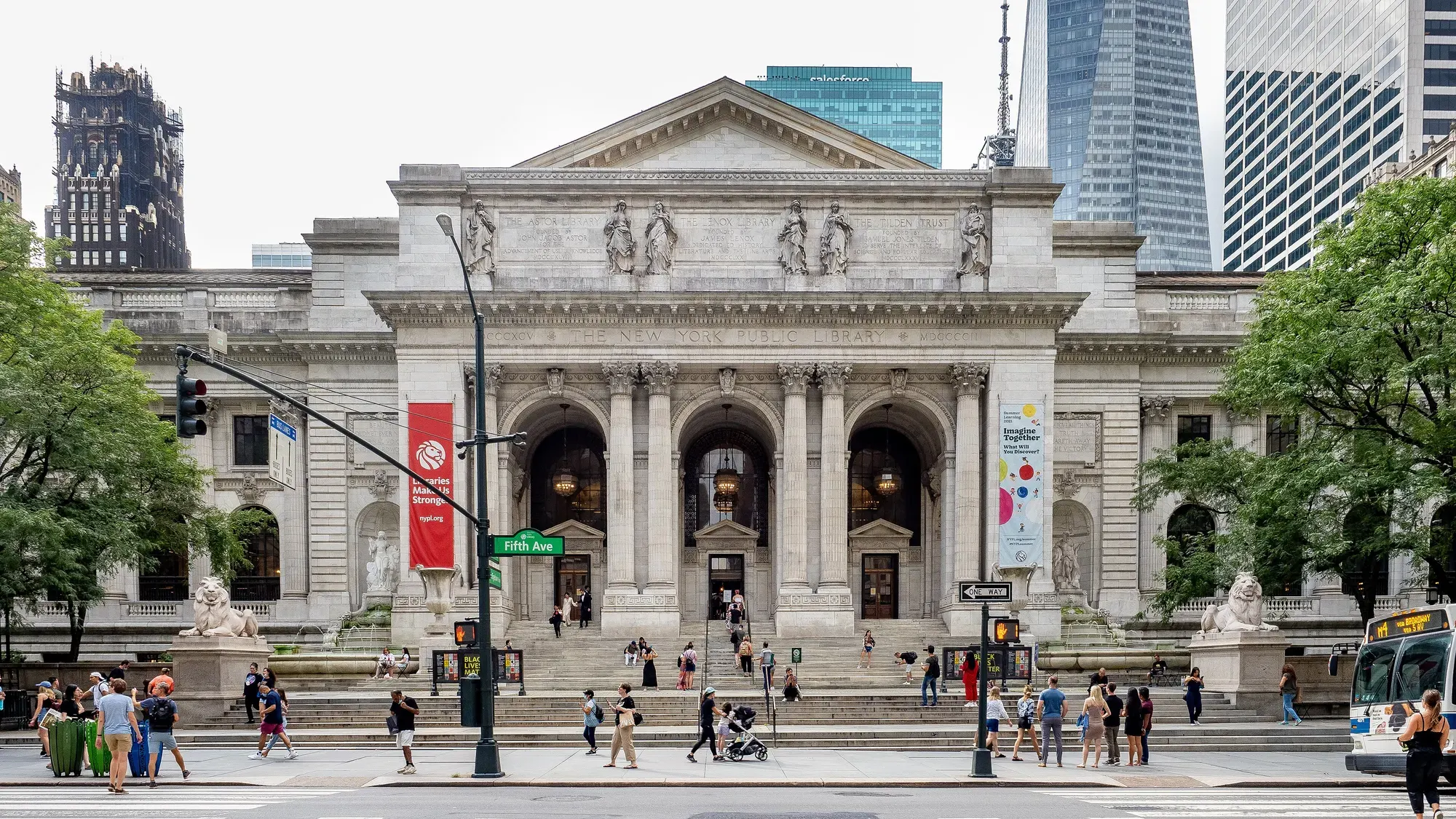 The white marble Beaux-Arts façade of the New York Public Library on Fifth Avenue, with arched entrances, stone lions and people on the steps