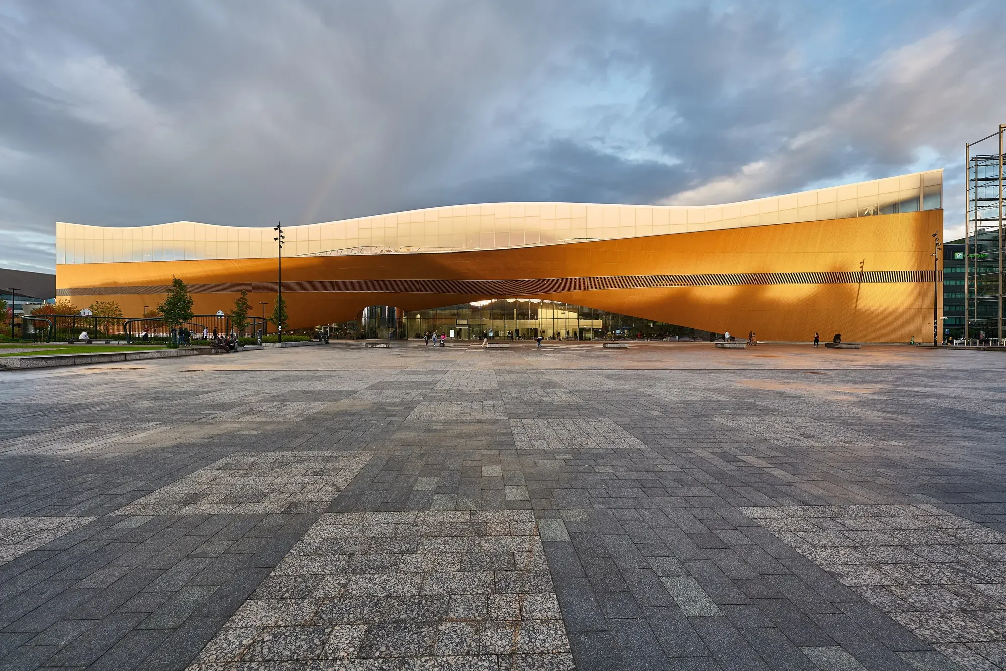 Oodi seen from the square at dusk, its curved timber-clad facade lit from within