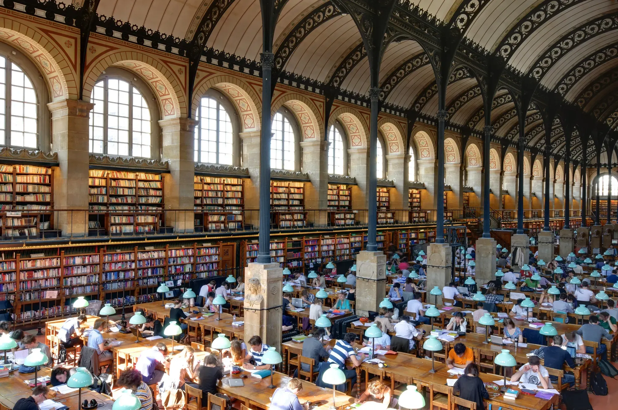 Readers at long tables in the reading room of the Sainte-Geneviève Library, beneath a line of cast-iron arches