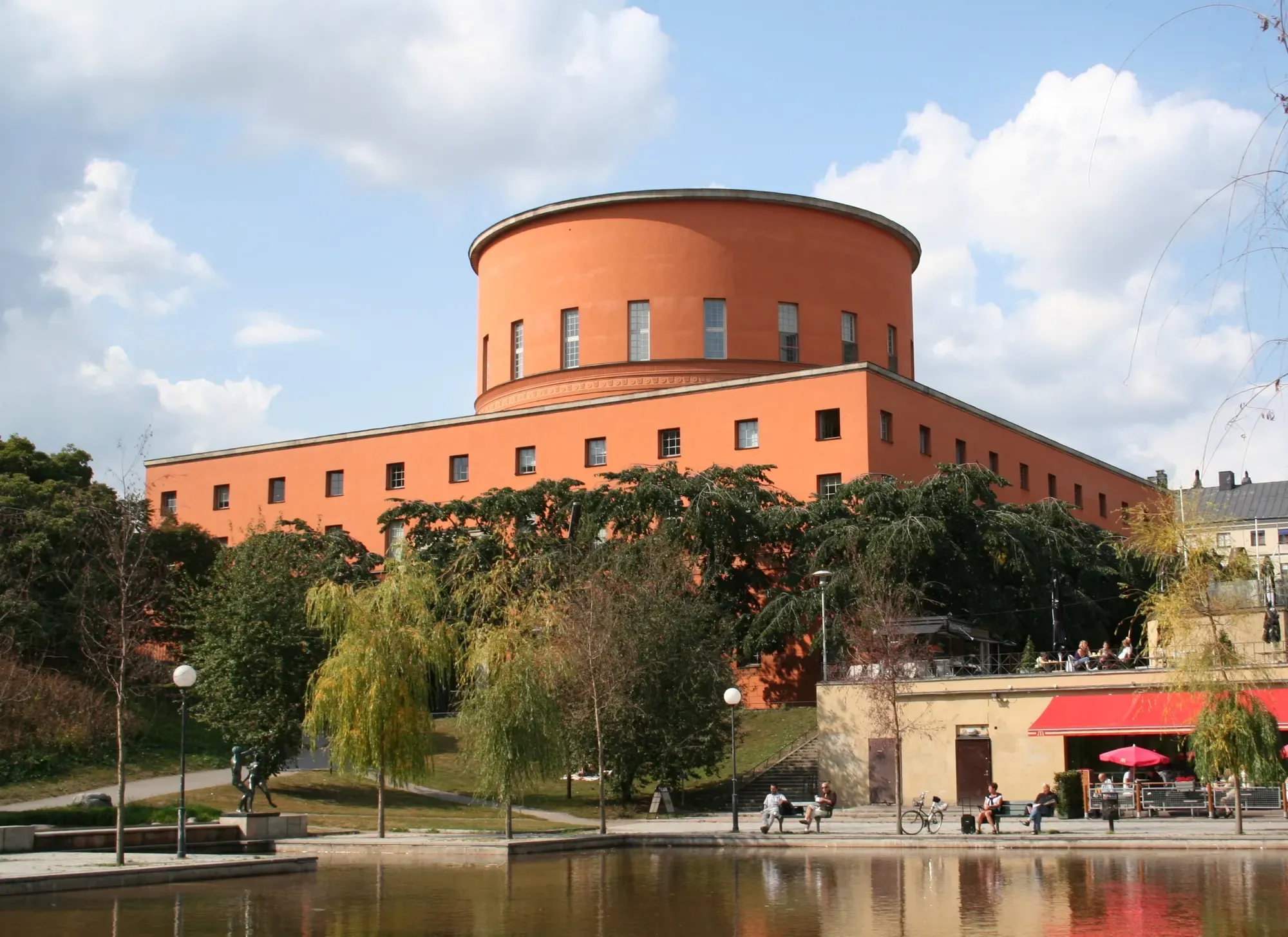 Asplund's orange-rendered rotunda rising from a low rectangular block, with trees and water in the foreground