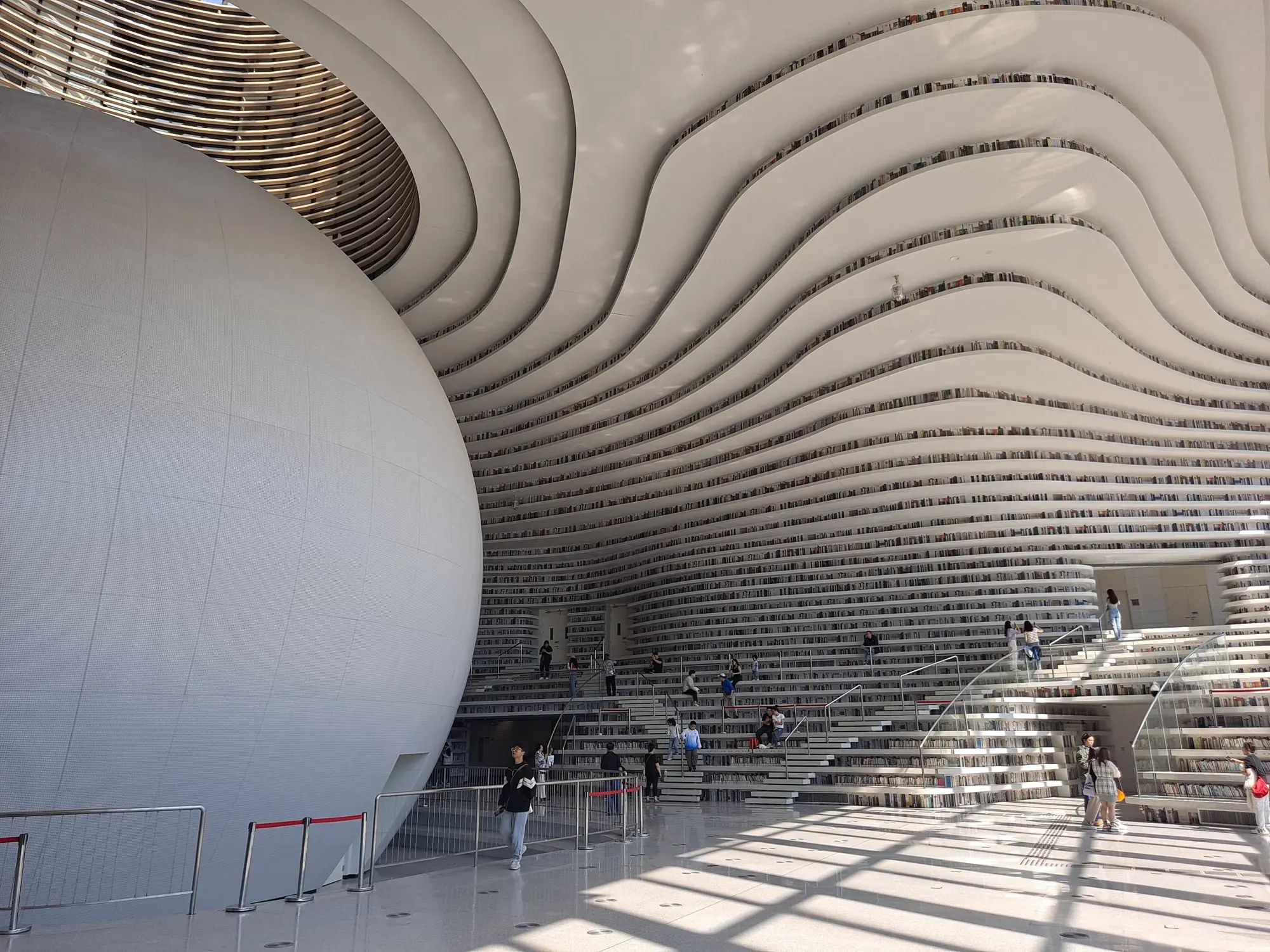 A huge white luminous sphere in the library atrium, surrounded by wave-like white terraces of bookshelves